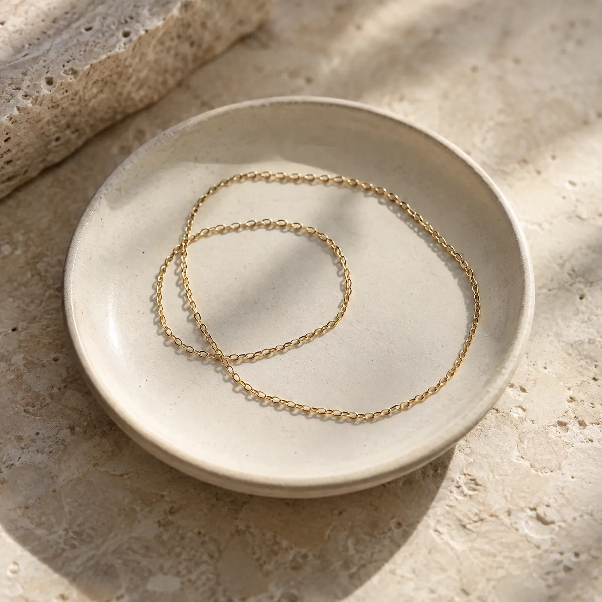 Delicate gold bracelet and anklet chains on a cream dish